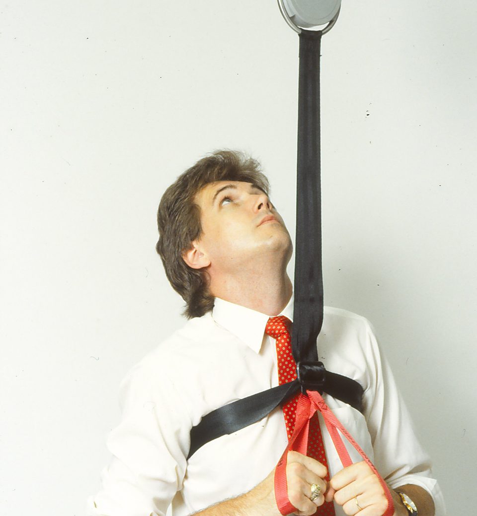 Rick Denzien in a white shirt and red tie wearing the harness, looking up along the black strap toward the unit
