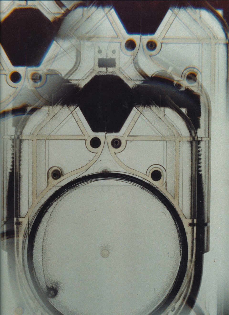 X-ray view of the inside of an Exit Traveler unit: a moulded ribbed frame with round fittings, dark six-sided shapes in the upper part and the round tape cassette, shown empty, in the lower half