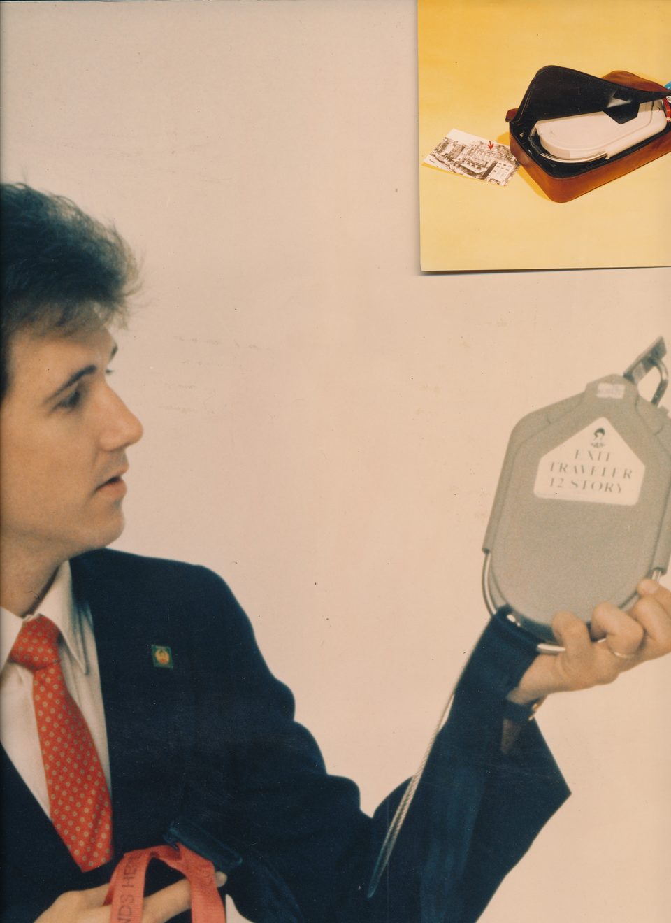 Showboard image of Rick Denzien in a dark jacket holding the grey Exit Traveler unit, with a small picture of the kit pinned at the top